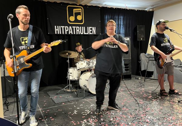Hitpatruljen giver et nummer for de fremmødte foran et sort banner med "Hitpatruljen".